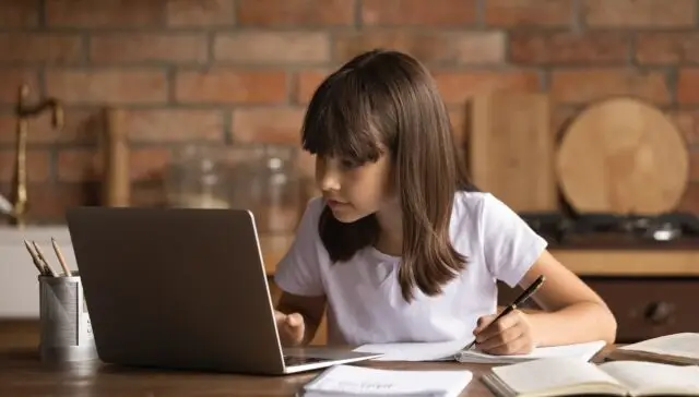 Skupiona dziewczynka podczas nauki zdalnej w domu korzystająca z laptopa do odrabiania lekcji